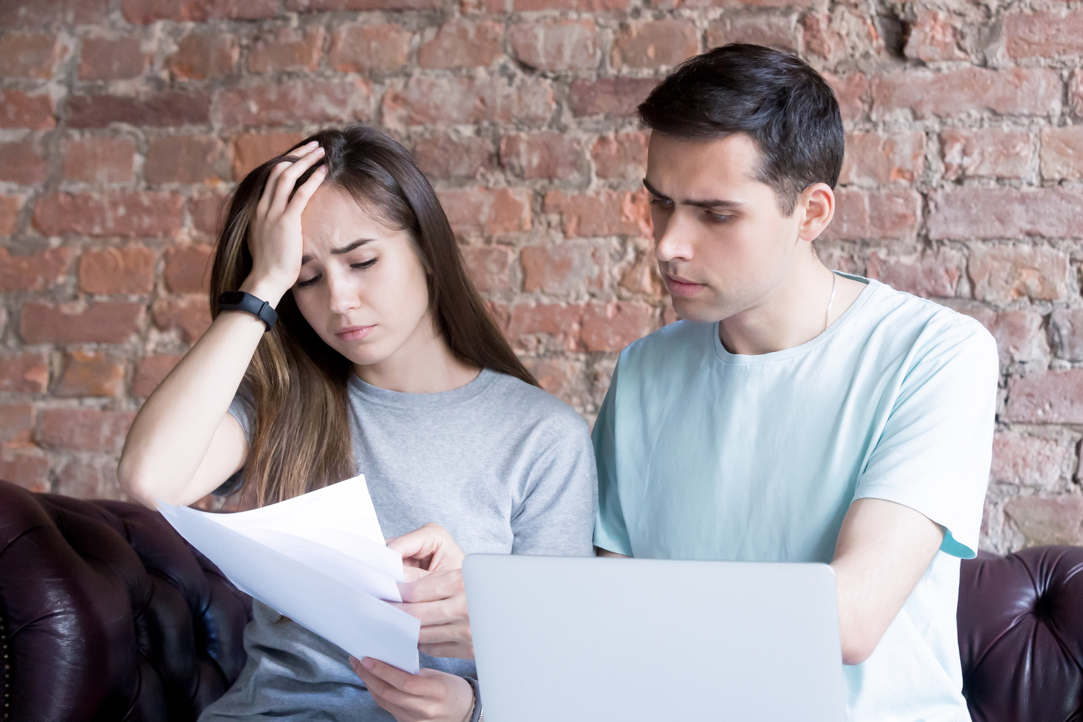 Distressed young couple reviewing paper work on sofa.