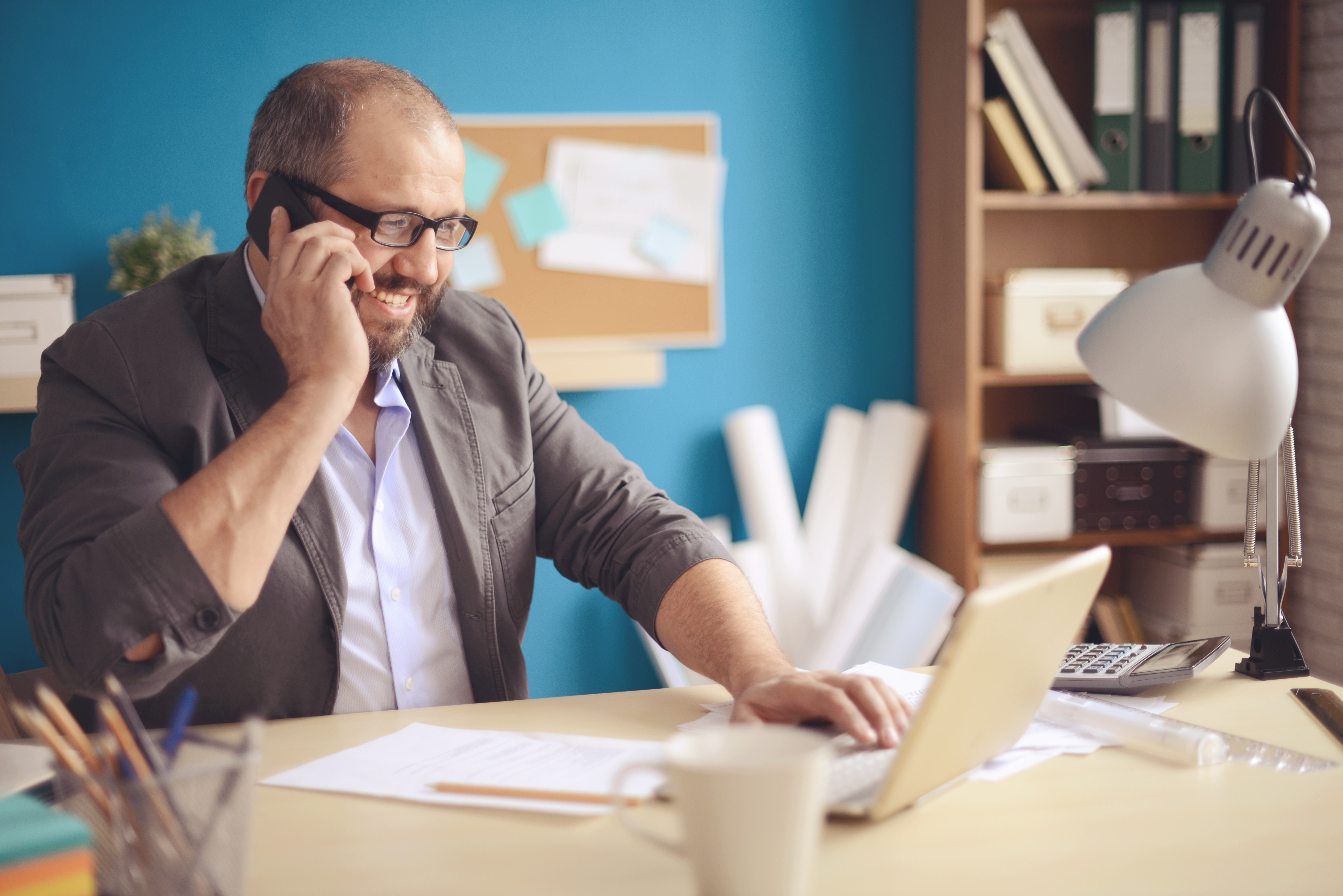 guy with glasses smiling at laptop on phone