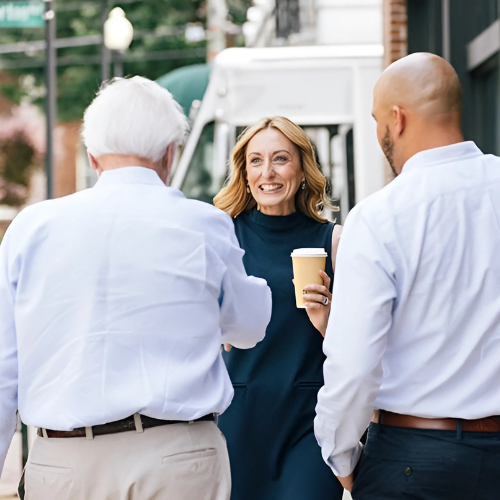 business banking lady shaking older man's hand while smiling with coffee and another man next to her