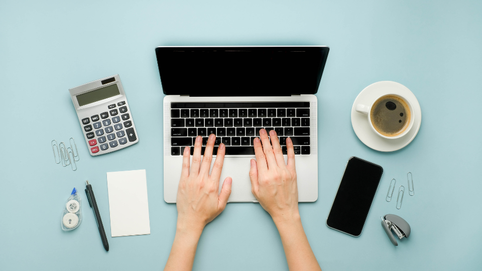 person typing on laptop - phone, stapler, calculator around it