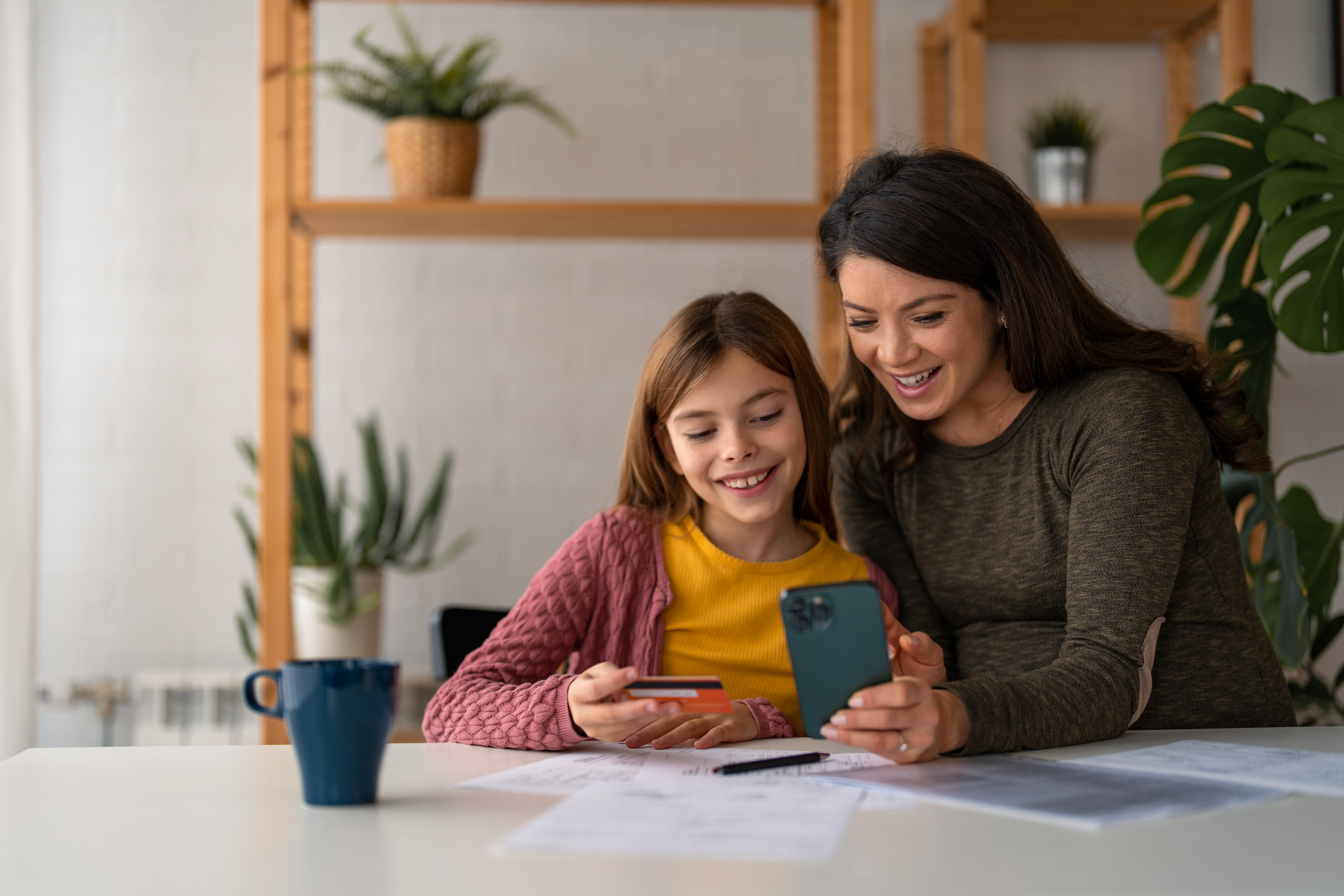 daughter and mom looking at phone and debit card smiling