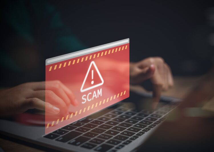 hands on laptop with scam alert in red