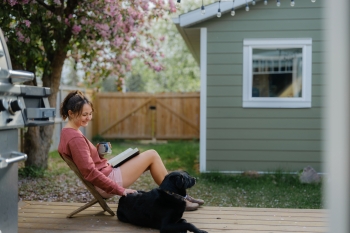 Young female homeowner sitting on her porch petting her black lab Banner