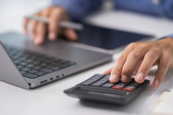 typing on laptop with calculator next to it Banner