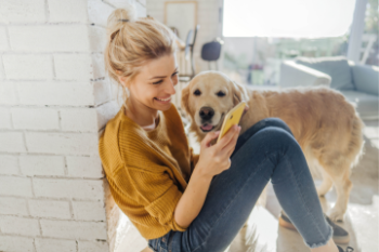 blonde younger woman smiling on phone with golden retriever next to her Banner