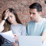 Distressed young couple reviewing paper work on sofa.