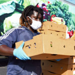 Volunteer in mask and gloves unloading produce boxes from truck.