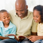 Dad with son and daughter sitting on either side of him reviewing a book together.