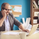guy with glasses smiling at laptop on phone