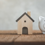 white piggy bank with small wooden house next to it istock