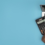 blue background with hands on calculator, notebook, and laptop