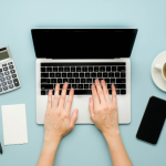 person typing on laptop - phone, stapler, calculator around it