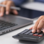 typing on laptop with calculator next to it